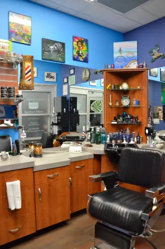 A corner of the barbershop. A barber's chair, a collection of colorful paintings - many of which reference Alice in Wonderland, tools, and haircare products can be seen.