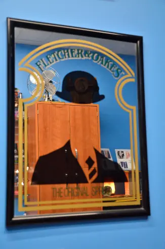 An image of a novelty mirror with a screenprinted top hat an suit inviting onlookers to align their reflection with the attire on the mirror.