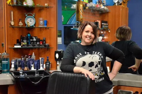 Amy the barber standing next to her barber's chair.
