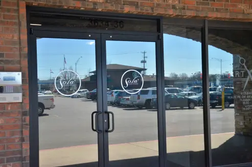The glossy front doors of Sola Salons that have a screenprinted logo consisting of a circle with the word 'Sola'.