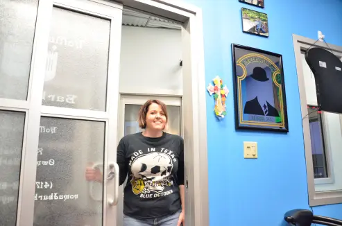 Amy welcoming someone through the door while wearing a shirt with a skull that reads 'Made in Texas'.