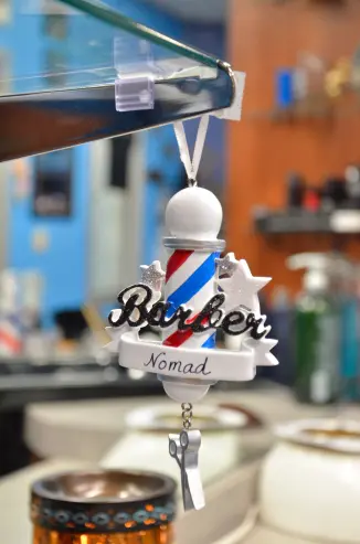 A miniature ornamental barber's pole hanging from a shelf that reads 'Nomad'.